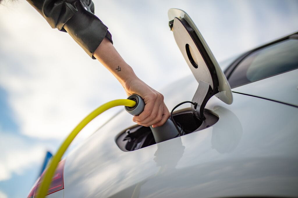 Low angle close-up shot of the hand of a woman holding a charging plug while charging an EV