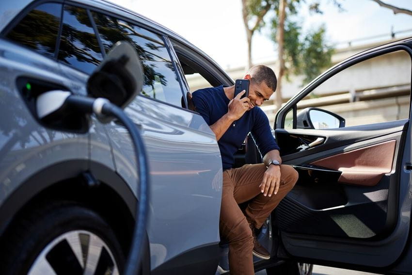 miling man talking on smart phone sitting in electric car